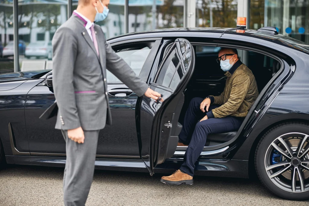 Man in eyeglasses stepping out of a chauffeur-driven executive car