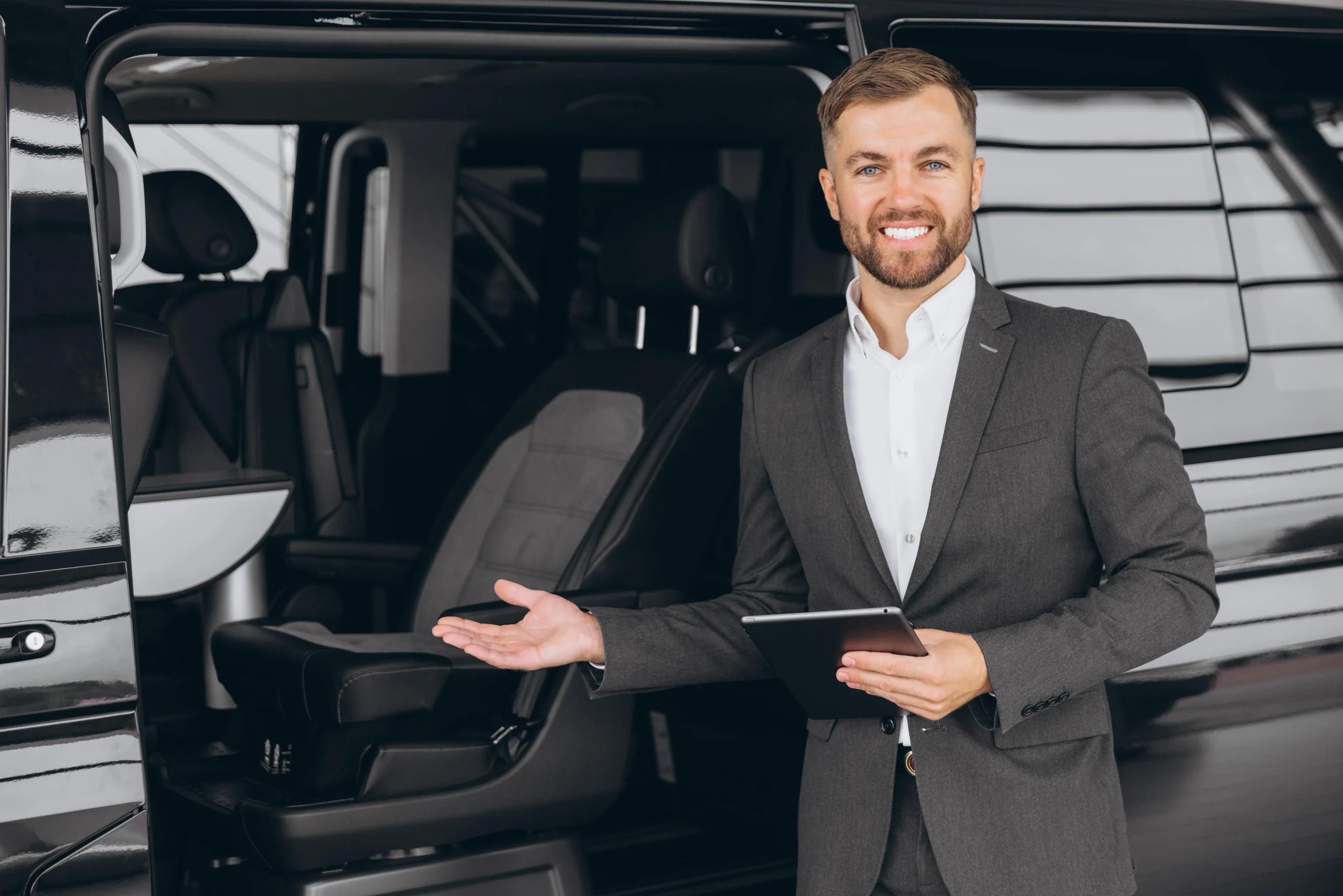 smiling-friendly-car-seller-in-suit-standing-in-ca-2025-02-16-21-26-02-utc-min